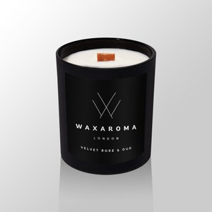 May include: Black candle jar with a white wax top and a wooden wick. The jar has a black label with the text "WAXAROMA LONDON VELVET ROSE & OUD".