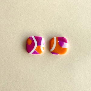 Op de afbeelding: Een paar vierkante oorbellen met een geometrisch patroon in roze, oranje en witte tinten.