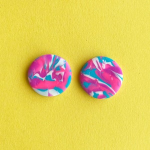 Op de afbeelding: Een paar ronde, roze, blauwe en witte marmeren oorbellen. De oorbellen zijn gemaakt van polymer clay en hebben een swirl-patroon.