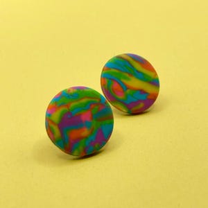 Op de afbeelding: Een paar kleurrijke, ronde oorbel studs met een draaiende, abstracte print in tinten groen, blauw, paars, oranje en geel.