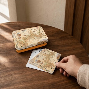 May include: A rectangular metal storage tin with a tan and brown Grand Canyon National Park map illustration on the lid, accompanied by a deck of playing cards featuring the same map design, with one card showing the Jack of Spades symbol.