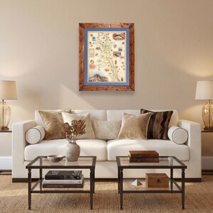 May include: A framed map of Capitol Reef National Park featuring a cream-colored background with detailed illustrations of the landscape, enclosed in a blue mat and a rustic brown wooden frame, displayed on a wall above a white sofa.