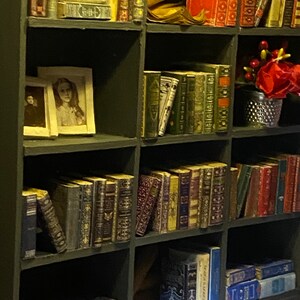 Vintage-style framed portraits, carefully arranged miniature books, and mirrored details create depth, warmth, and character in the cozy library atmosphere.
