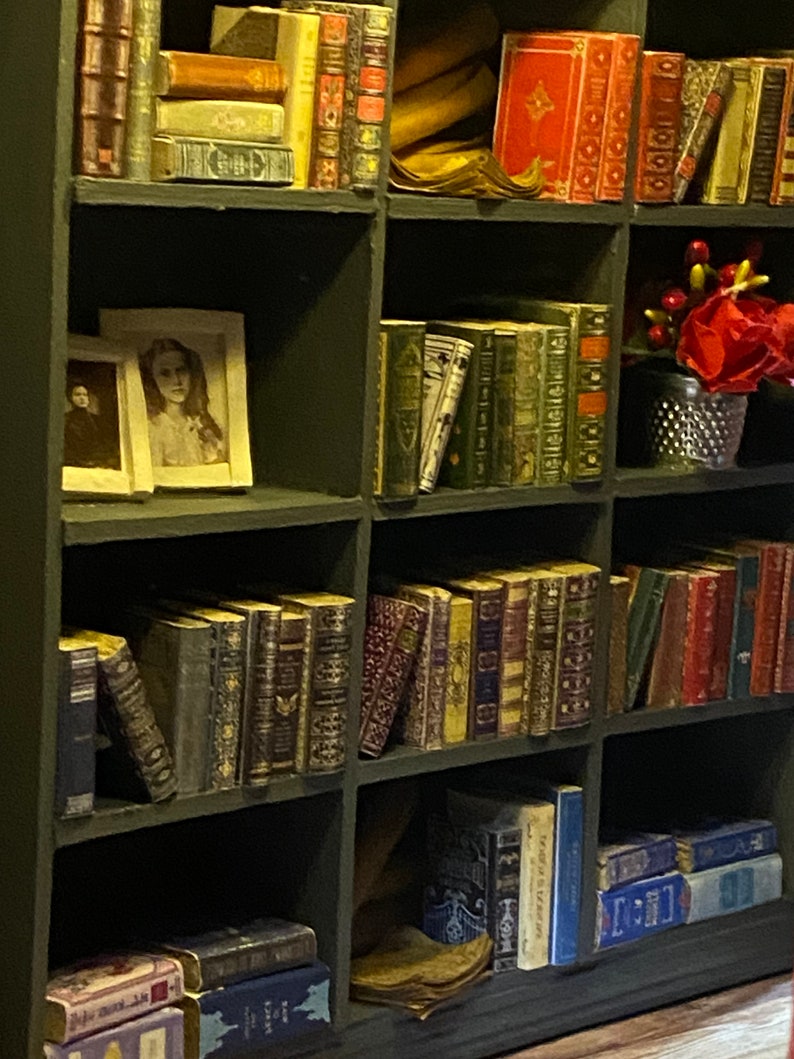 Vintage-style framed portraits, carefully arranged miniature books, and mirrored details create depth, warmth, and character in the cozy library atmosphere.
