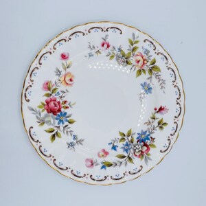 May include: White porcelain plate with a scalloped edge and a gold rim. The plate is decorated with a floral pattern featuring pink, red, yellow, and blue flowers with green leaves. The design is symmetrical and elegant.