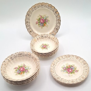 Può includere: Un set di piatti vintage color crema con un motivo floreale a rose. I piatti e le ciotole hanno un bordo in filigrana dorata. Il set include piatti e ciotole più piccole, perfetti per servire un pasto.