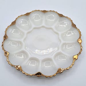 May include: White, scalloped egg serving dish with a gold rim. The dish has 12 individual egg compartments surrounding a central serving area. The gold rim adds a touch of elegance to this vintage-style serving piece.