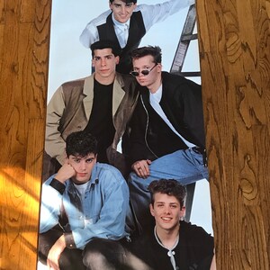 Könnte beinhalten: Ein Vintage-Poster mit einer Gruppe von fünf jungen Männern, die alle Freizeitkleidung tragen. Das Poster ist weiß mit rotem Text, der "New Kids on the Block" lautet.