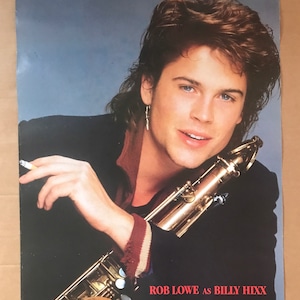 May include: Poster featuring Rob Lowe as Billy Hixx in St. Elmo's Fire. Lowe is holding a saxophone, wearing a black jacket with a burgundy collar and striped cuffs. The poster has a blue background.