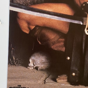May include: A close-up of a movie poster for the film "The Beastmaster". The poster features a skull on the ground and a person's leg and sword in the background.