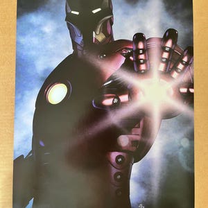 Op de afbeelding: Een rood en zwart Iron Man-pak met een gloeiend licht in de palm van de hand. De tekst "STARK INDUSTRIES PROTOTYPE LAUNCHING MAY 2 2008" staat onderaan de poster.