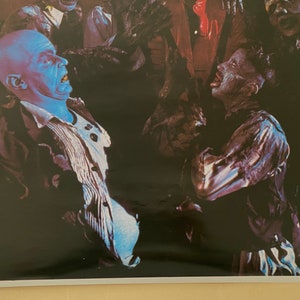 May include: A black and white image of a scene from a horror movie. A man with a blue face is being attacked by a group of zombies.