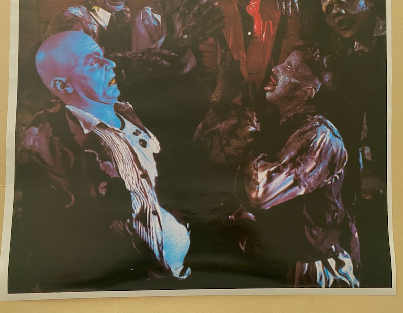 May include: A black and white image of a scene from a horror movie. A man with a blue face is being attacked by a group of zombies.