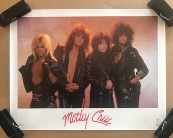 May include: A vintage poster featuring a band called "Mötley Crüe". The poster shows five members of the band in black leather jackets, with a pink and red background.