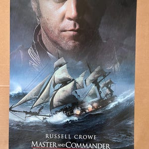 May include: A movie poster for the film "Master and Commander: The Far Side of the World" starring Russell Crowe. The poster features a close-up of Crowe's face with a large sailing ship in the background. The poster is set against a stormy sea with a dark blue and gray color scheme.