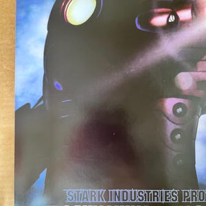 Op de afbeelding: Een zwart en zilveren poster met een futuristisch robotontwerp. De poster heeft de tekst "STARK INDUSTRIES PRO... LAUNCHING MAY 2" onderaan.