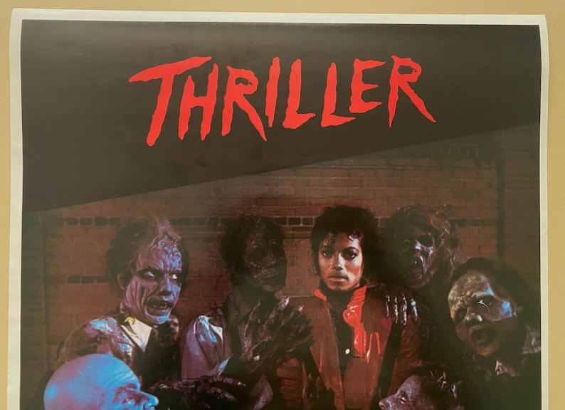 May include: A vintage poster for Michael Jackson's Thriller album. The poster features a red and black color scheme with the word "Thriller" in large red letters at the top. The poster also features a group of zombies surrounding Michael Jackson, who is wearing a red jacket.