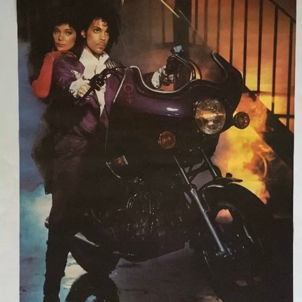 Op de afbeelding: Een vintage poster voor de film Purple Rain, met Prince en Apollonia op een motorfiets. De poster heeft een paars en geel kleurenschema en de titel "Purple Rain" is geschreven in een vet, gestileerd lettertype.