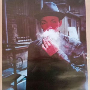 May include: A black and white poster featuring a man wearing a black fedora and a black jacket. He is smoking a cigarette and exhaling smoke. The poster has the text "TRICKY PRE-MILLENNIUM TENSION" in white letters.