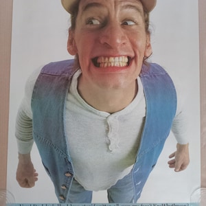 Puede incluir: Un hombre con un chaleco vaquero azul sobre una camiseta blanca y pantalones vaqueros azules mira a la cámara con una amplia sonrisa. Lleva una gorra de béisbol y tiene una expresión confusa en su rostro. El texto "Vern! Do I look like I have stupid written all over my face? KnoWhutlmean?" está escrito en la parte inferior de la imagen.