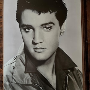 May include: Black and white portrait of Elvis Presley wearing a jacket with a zipper and a button. He is looking directly at the camera.