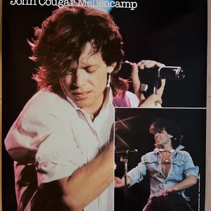 Op de afbeelding: Een zwart-wit poster met een foto van John Cougar Mellencamp die op het podium optreedt. De poster heeft de tekst "John Cougar Mellencamp" bovenaan.