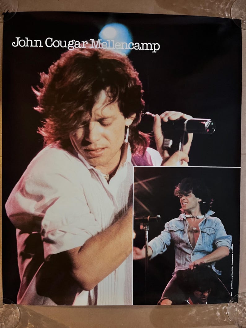 Op de afbeelding: Een zwart-wit poster met een foto van John Cougar Mellencamp die op het podium optreedt. De poster heeft de tekst "John Cougar Mellencamp" bovenaan.