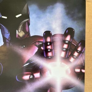 Op de afbeelding: Een close-up van een rood en zilveren Iron Man-figuur met een gloeiende repulsorstraal in zijn hand. Het figuur is geposeerd in een dynamische actiehoud, met zijn arm naar voren gestrekt. De achtergrond is wazig, blauw en paars.