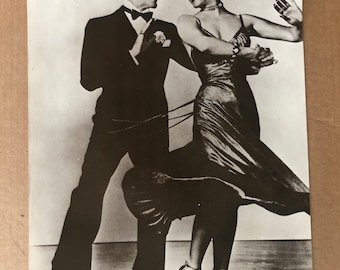 Può includere: Fotografia in bianco e nero di un uomo e una donna che ballano. L'uomo indossa uno smoking con papillon e la donna un abito lungo e tacchi alti. Si sorridono.