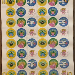 May include: A large rectangular sheet featuring a grid of circular stickers with Cabbage Patch Kids branding. The stickers display various illustrations including dolls, storks carrying bundles, and the Cabbage Patch Kids logo in yellow and blue.