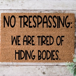 May include: A brown doormat with the text "NO TRESPASSING: WE ARE TIRED OF HIDING BODIES."