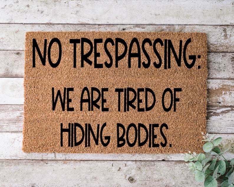 May include: A brown doormat with the text "NO TRESPASSING: WE ARE TIRED OF HIDING BODIES."