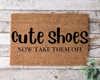May include: A brown coir doormat with the text "cute shoes now take them off" in black lettering.