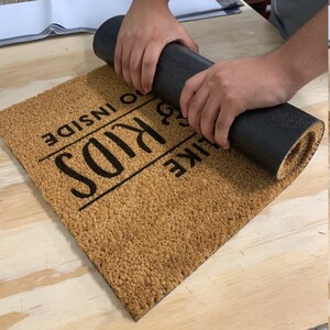 May include: A brown coir doormat with the text "Like Kids Go Inside" in black lettering.