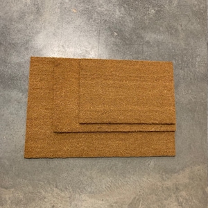 May include: Three brown coir doormats of different sizes stacked on top of each other.