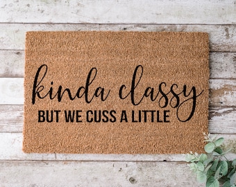 May include: A brown coir doormat with the text "kinda classy but we cuss a little" in black cursive lettering.