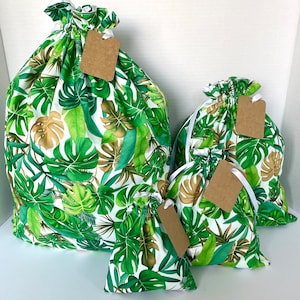 May include: Four green and white drawstring bags with tropical leaf patterns and brown paper tags. The bags are different sizes and are arranged in a pyramid shape.