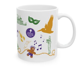 May include: White ceramic mug with a colorful design featuring New Orleans icons, including a fleur-de-lis, a pelican, a Mardi Gras mask, a musical note, a voodoo doll, a hurricane evacuation route sign, and a steamboat.