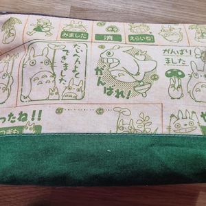 May include: A green and beige zippered pouch with a cartoon character print. The pouch features Japanese text and illustrations of a flying creature with large ears.