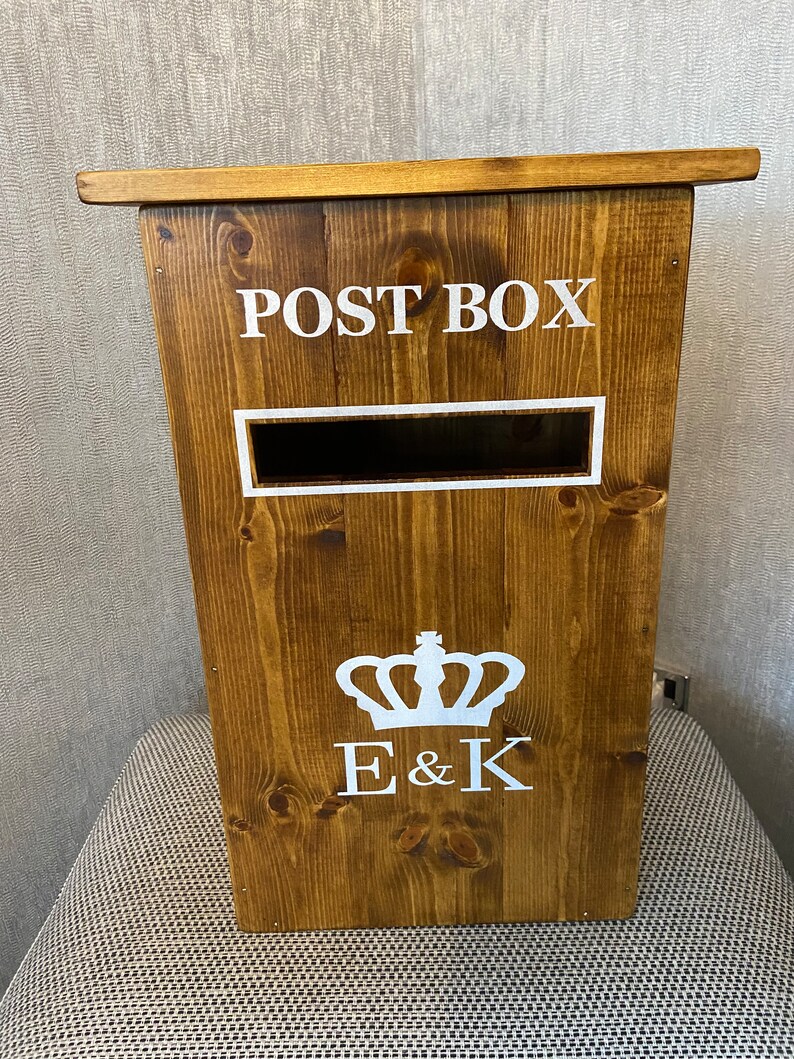 May include: A wooden post box with a white "POST BOX" sign, a white crown, and the initials "E & K" on the front.