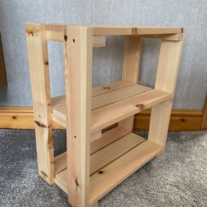 May include: A natural wood shelf unit with two shelves. The shelf unit is made of unfinished pine wood and has a rustic look.