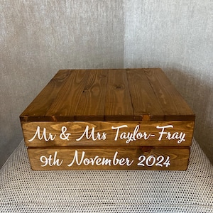 May include: Two-tiered wooden cake stand with a rustic brown finish. The top tier has a smooth surface, while the bottom tier has the text "Mr & Mrs Taylor-Fray 9th November 2024" in white.