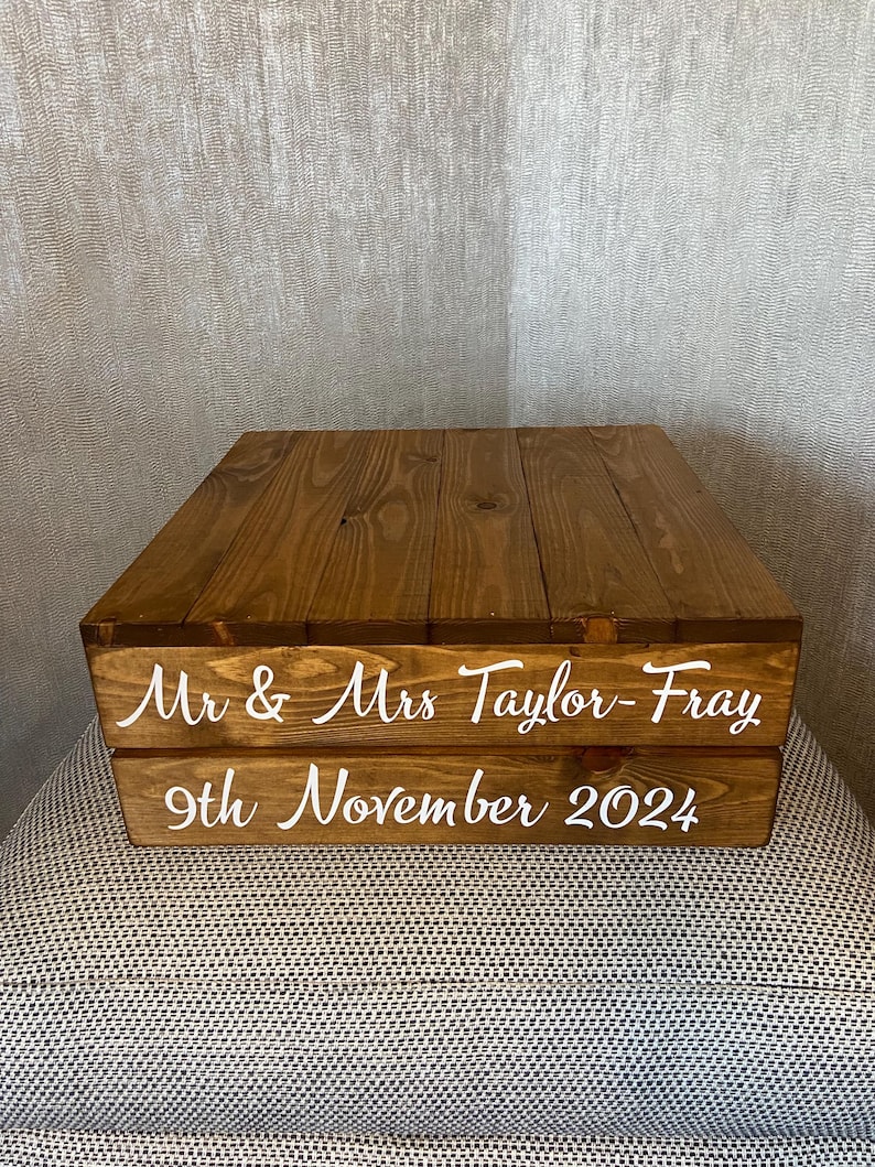 May include: Two-tiered wooden cake stand with a rustic brown finish. The top tier has a smooth surface, while the bottom tier has the text "Mr & Mrs Taylor-Fray 9th November 2024" in white.