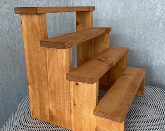 May include: A wooden tiered display stand with four shelves. The stand is made of natural wood and has a light brown stain. The shelves are all the same size and are evenly spaced.