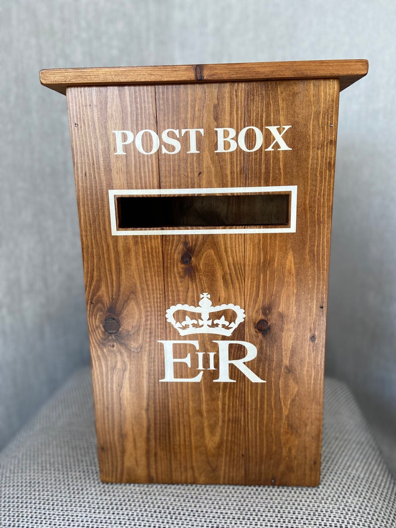 May include: A wooden post box with a white "POST BOX" inscription and a royal crest with "E II R" in white lettering.