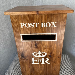 May include: A wooden post box with a white "POST BOX" inscription, a white slot for mail, and a white "EIIR" royal crest with a crown.