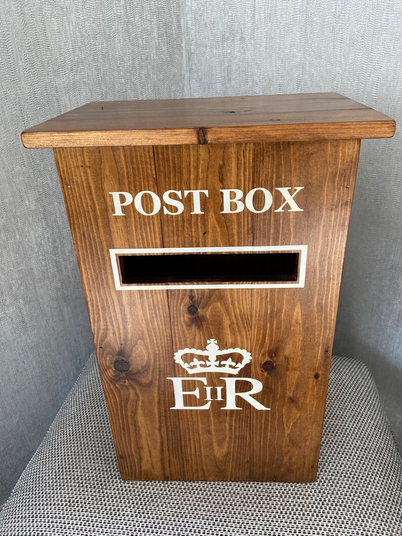 May include: A wooden post box with a white "POST BOX" inscription, a white slot for mail, and a white "EIIR" royal crest with a crown.