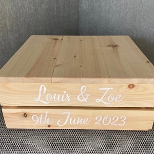 May include: A wooden cake stand with the names "Louis & Zoe" and the date "9th June 2023" written on it.