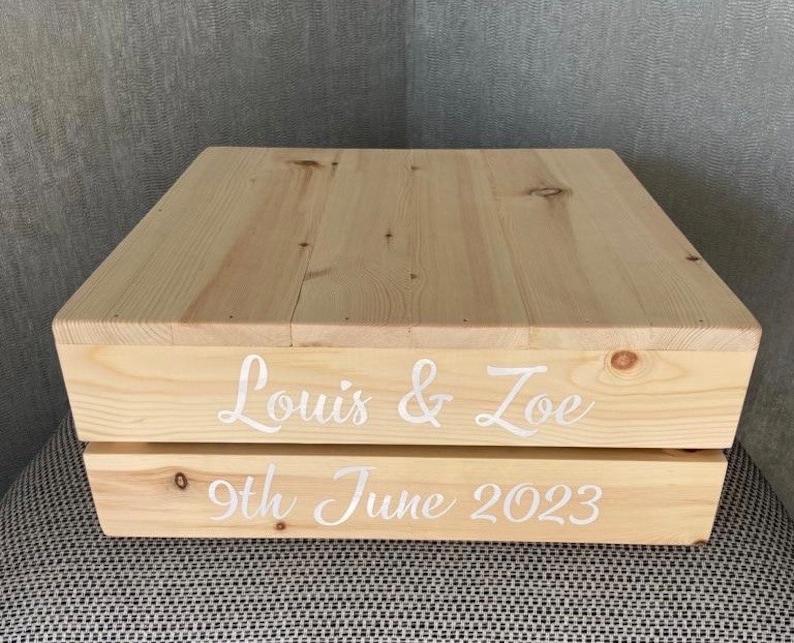 May include: A wooden cake stand with the names "Louis & Zoe" and the date "9th June 2023" written on it.