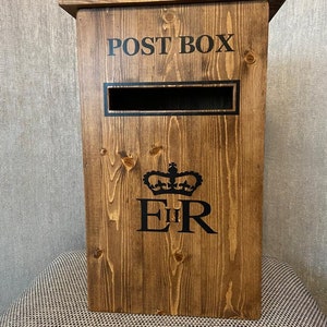 May include: A wooden post box with a slot for mail. The box is painted brown and has the words "POST BOX" printed on the front. The box also has a royal crown and the letters "E II R" printed on the front.